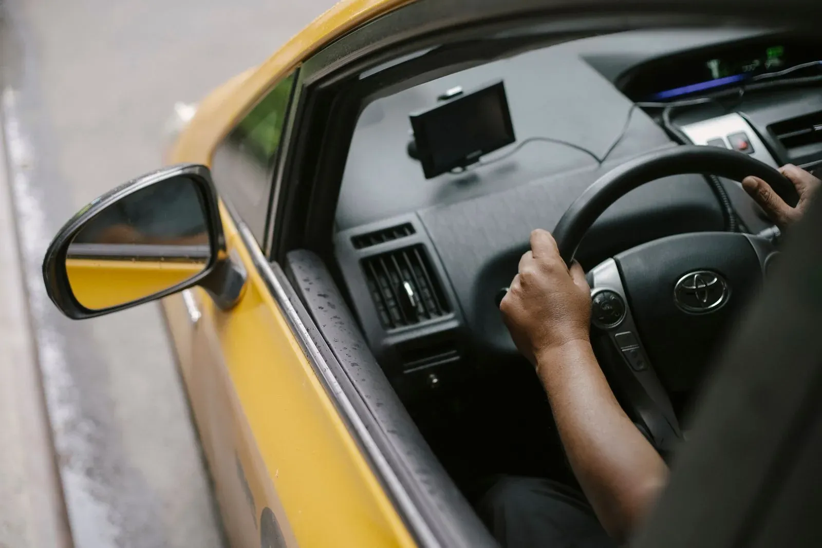 A driver's hands on the steering wheel of a yellow taxi